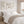 A triptych of watercolor paintings featuring delicate branches and leaves in soft shades of green and brown. The paintings are framed and displayed on a white wall above a bed.  The artwork creates a calming and elegant atmosphere in the bedroom.