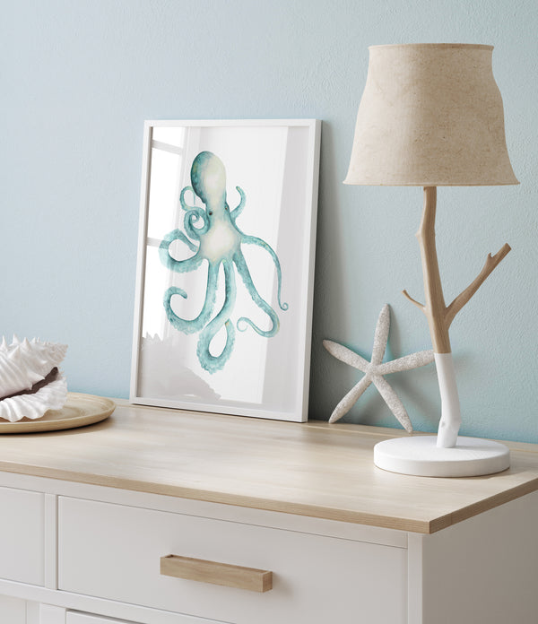 A framed watercolor painting of an octopus with vibrant blue and green colors. The artwork is displayed on a dresser with a lamp, seashells, and a starfish.