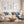 A styled living room featuring a white sofa with blue and beige patterned pillows, a round wooden coffee table, a beige armchair, and three framed botanical wall art showing minimalist blue botanical with navy blue branches prints above the sofa.
