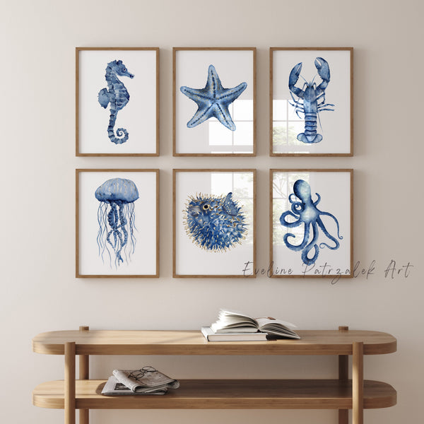 Set of six framed ocean-themed prints including lobster, tropical fish, starfish jellyfish and octopus hang above a wooden console table.