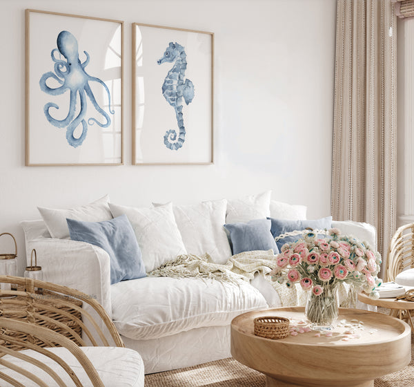 Set of 2 octopus and seahorse wall art prints in wooden frames – coastal watercolor sea life artwork styled above white sofa with blue cushions and pink floral decor
