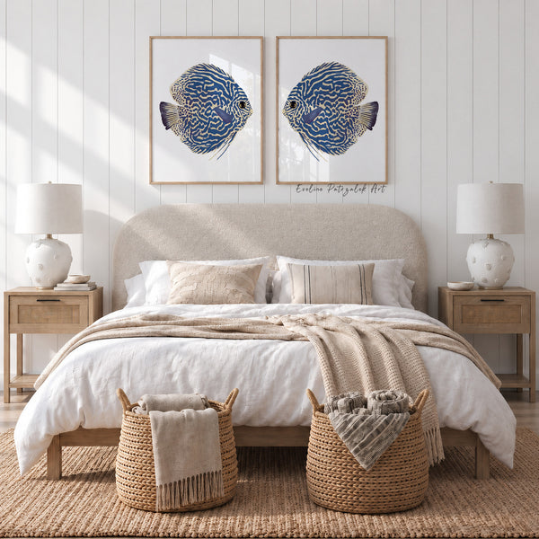 A styled bedroom scene with a bed dressed in white bedding and a beige throw blanket, flanked by matching nightstands and lamps. Two framed blue-and-gold fish wall art prints hang above the headboard, and two woven baskets sit at the foot of the bed.