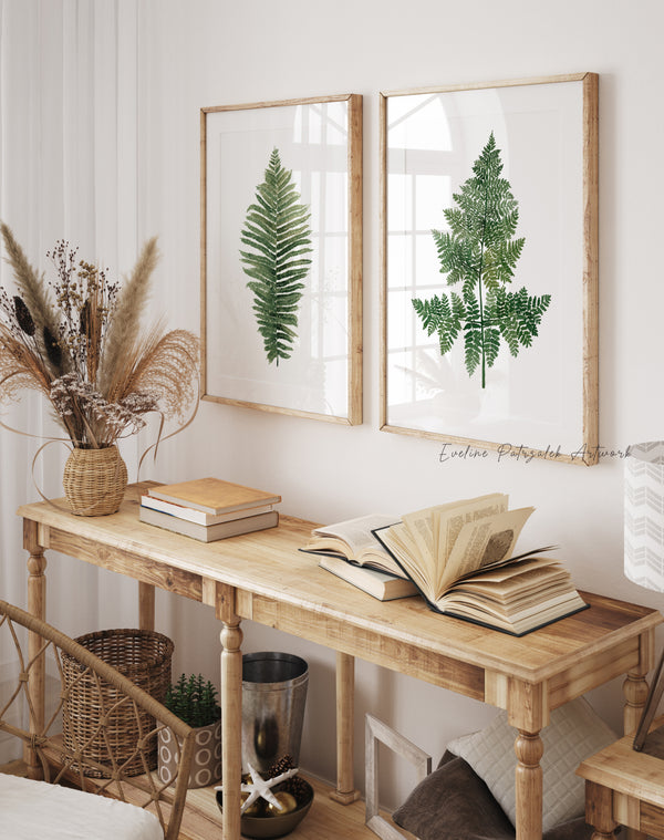 Nestled corner with a wooden table, books, and framed fern prints on a white wall.