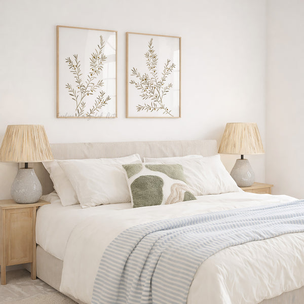 Neatly made bed with decorative pillows, 2 wooden frames above bed showing minimalist olive branches and lamps in a bedroom setting. 
