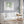 A watercolor painting of hanging green leaves adds a touch of nature to a living room with a white sofa, a round coffee table, and a gray wall.