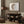 A framed watercolor painting of a moon in warm brown and beige tones with birds flying around it hangs above a wooden console table in a cozy living room with a neutral color palette.