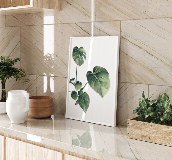 A watercolor painting of a green tropical leaf adds a touch of nature to a kitchen with a light colored countertop, wooden cabinets, and plants.