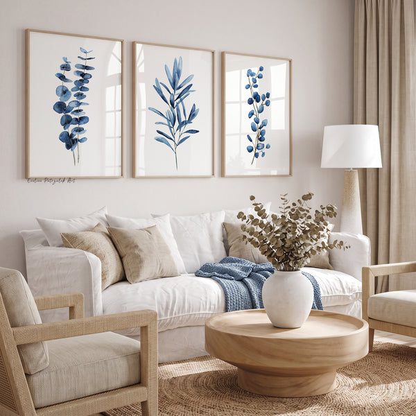 Navy blue botanical wall art set of 3 above a white linen sofa with beige cushions and a round wooden table