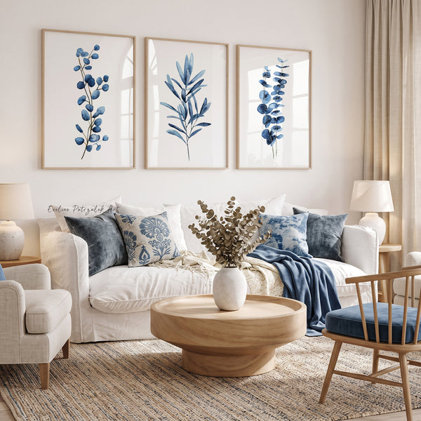Three navy blue eucalyptus and leaf branch prints above a white sofa with blue cushions