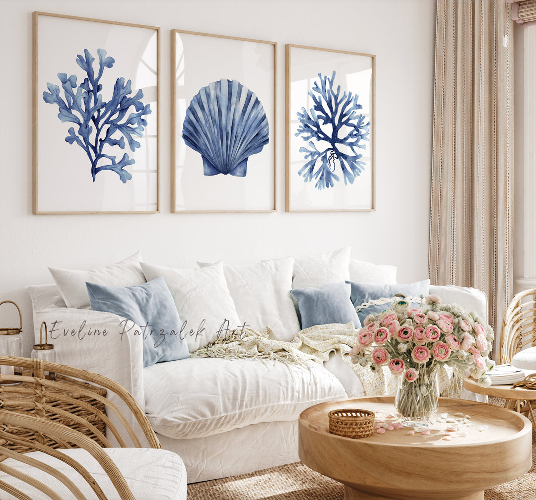 Living room with framed blue coral and shell art on the wall, white sofa, and wooden coffee table with flowers.