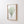 Close-up of the sage green sea fan print in an oak frame on a white panelled wall