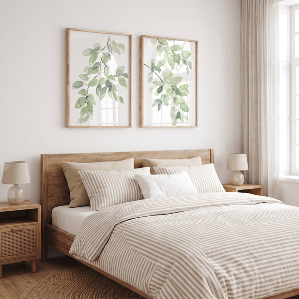 Two sage green watercolor leaf prints above a wooden bed with striped bedding