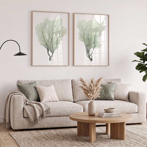 Pair of green sea fan prints in oak frames above a linen sofa and round wooden coffee table