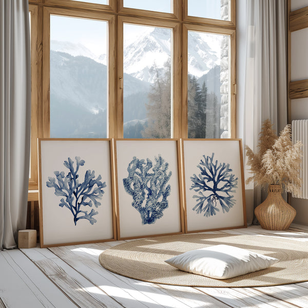 set of 3 frames with navy blue corals painted against white background stands on the floor and is leaning towards a large window with mountain view