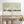 A pair of framed abstract landscape art prints in sage green and cream tones, displayed side-by-side on a distressed white console table in a bright, modern room.