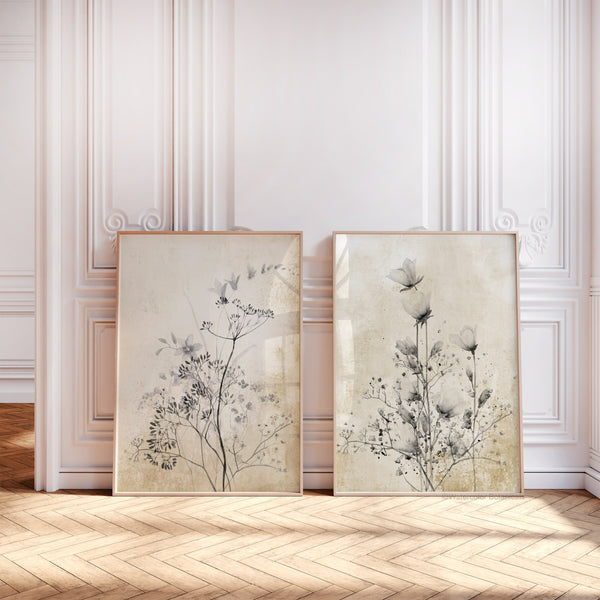 Two framed wildflower prints leaning against a panelled wall on a herringbone wooden floor