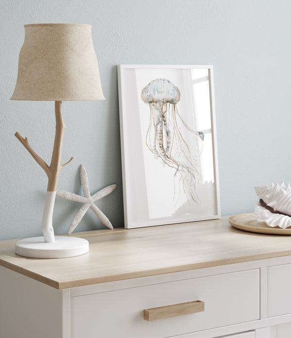 Watercolor jellyfish print in a white frame on a dresser with a starfish and a shell