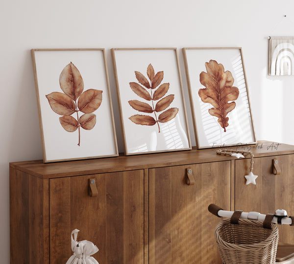 Three framed leaf prints on a wooden cabinet with a basket and decorative items.