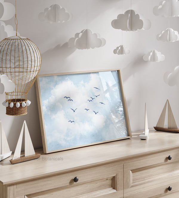 Framed artwork of birds flying in a sky with clouds on a wooden surface, surrounded by decorative items.