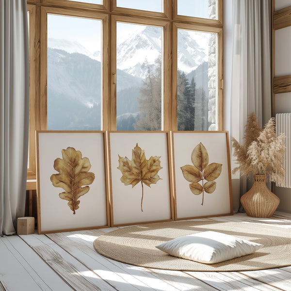 3 Holzrahmen mit gelben, aquarellierten Herbstblättern auf weißem Hintergrund stehen schräg auf dem Boden und sind an ein großes Fenster mit Blick auf die Berge gelehnt