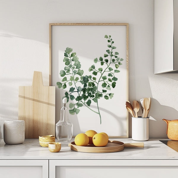 A framed watercolor painting showcases the intricate details of a green fern, creating a calming and elegant atmosphere above a kitchen counter with various kitchenware and fresh lemons.