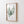 minimalist green fern leaf painting hangs in wooden frame viewed from an angled perspective 