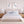 A styled bedroom scene with a bed dressed in white bedding and blue striped accents, flanked by matching nightstands and lamps, with two framed heron wall art prints above the headboard.