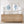 Wooden dresser with two framed shell art pieces and white lamps on a light wood floor.