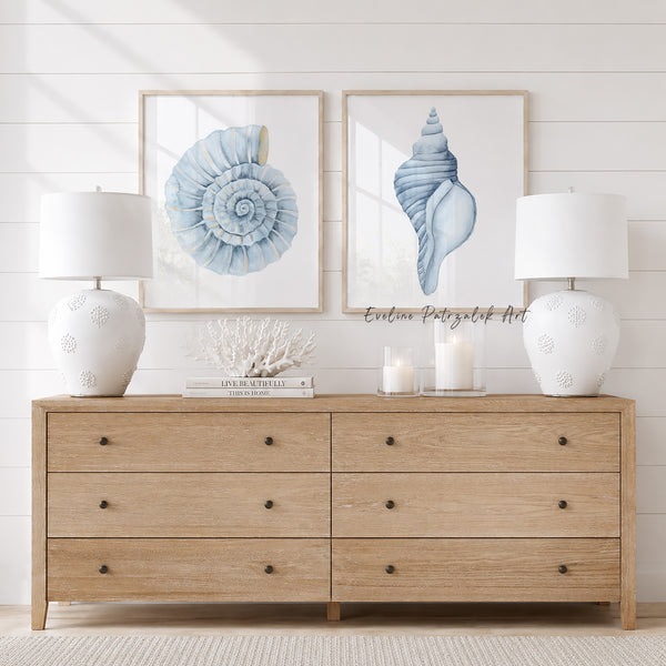 Wooden dresser with two framed shell art pieces and white lamps on a light wood floor.