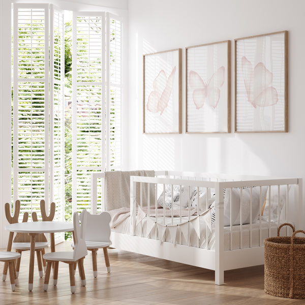A set of three framed watercolor paintings of delicate pink butterflies, arranged in a row on a light-colored wall in a child's bedroom. The butterflies are depicted with soft, ethereal details, creating a sense of lightness and airiness. The room features a white daybed with colorful bedding, a small table and chairs, and a rocking horse, creating a playful and inviting space for a child. The butterfly art adds a touch of whimsy and charm to the overall design.