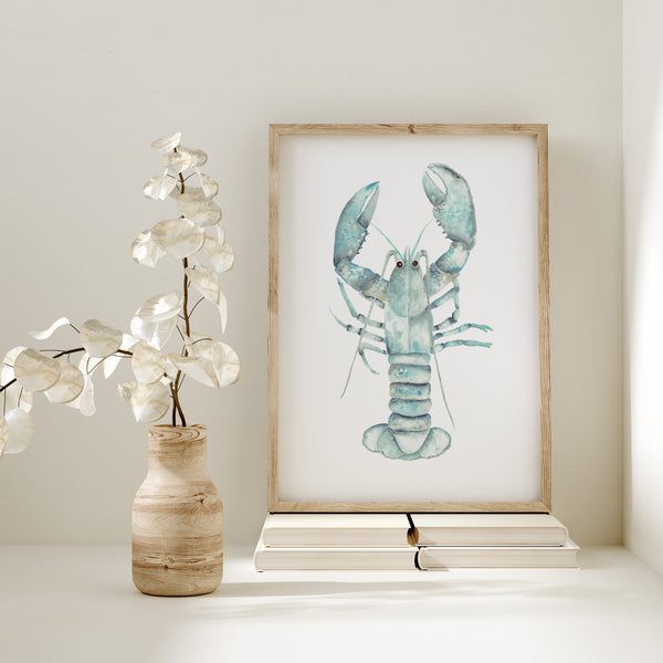 A framed watercolor painting of a lobster with vibrant blue and green colors. The artwork is displayed on a shelf with a vase of dried leaves and a stack of books.