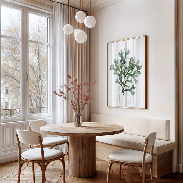 A framed watercolor painting showcases the intricate details of seaweed, adding a touch of nature to a dining area with a round wooden table, woven chairs, and a bench seat bathed in natural light streaming through a large window.