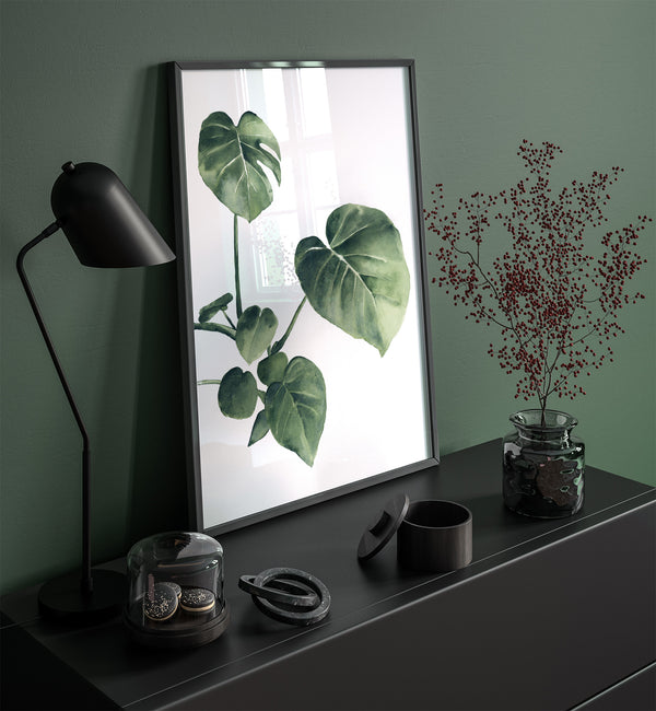 A watercolor painting of a green tropical leaf adds a touch of nature to a room with a dark green wall, a black lamp, and a black dresser.